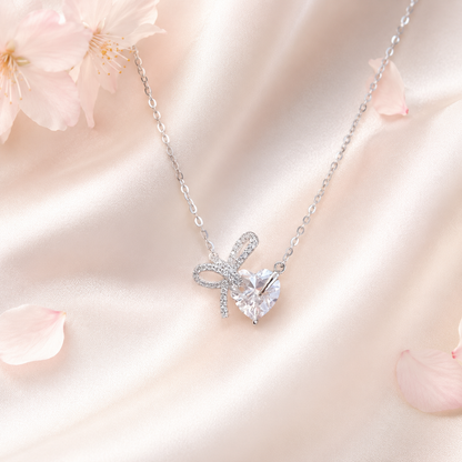 桜と淡いピンクの背景に置かれたTendre リボンハート モアサナイトネックレス
